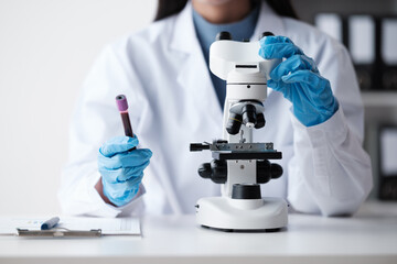Doctor hand taking a blood sample tube from a rack with machines of analysis in the lab background,...