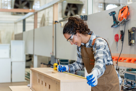 One Strong confident young aged women carpenter standing aim at wood plank in workshop. Latin female carpenter entrepreneur working craft with wood diy tool in workbench shop carpentry