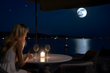 Back view young woman sitting in table at open cafe near the beach with beautiful moon in the night sky