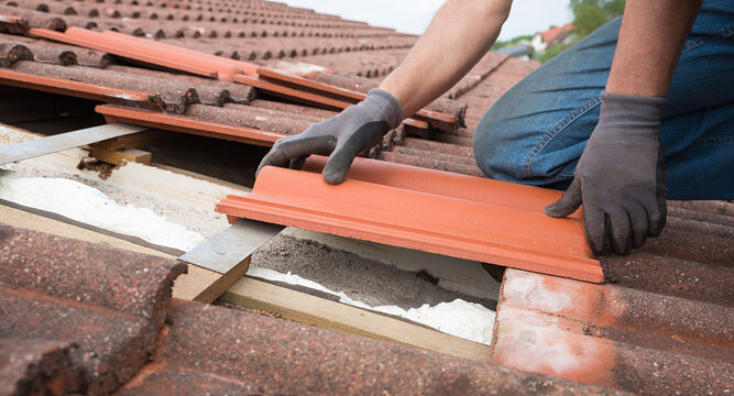 man fit in new roof shingels on the house rooftop, replacing damaged ones