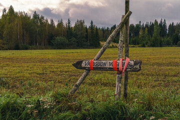 Fototapeta na wymiar Wooden sign of Vajosuon vaellus hiking trail with red tape next to a field in Kurjenrahka National Park