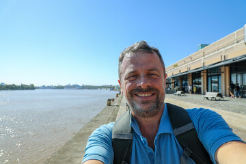 middle aged man taking a selfie phone on holidays bordeaux quay background - obrazy, fototapety, plakaty