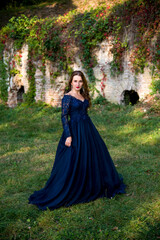 Beautiful brunette woman with curly hair and red lips in long blue dress  walking in the park