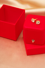 Stylish golden earrings in red box on beige silk background