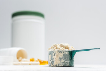 Whey protein powder in measuring spoon, white capsules of amino acids, vitamins and yellow capsules omega 3 on white background, healthy eating and bodybuilding food supplements