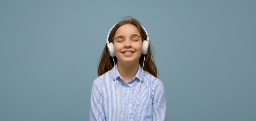 Listening to music. Satisfied teenage girl listens to music in headphones. A teenage girl in headphones listens to songs on a headset. Banner. light blue background - obrazy, fototapety, plakaty