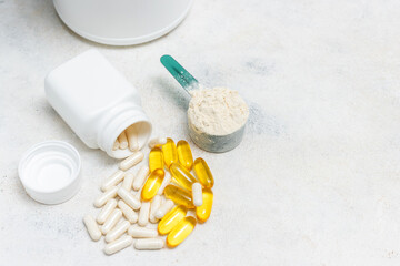 Whey protein powder in measuring spoon, white capsules of amino acids, vitamins and yellow capsules...