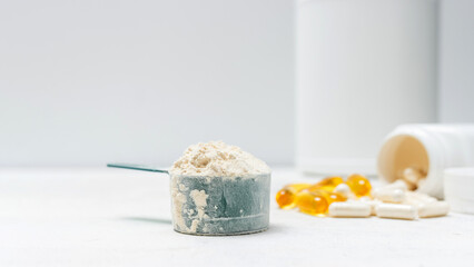 Whey protein powder in measuring spoon, white capsules of amino acids, vitamins and yellow capsules omega 3 on white background, healthy eating and bodybuilding food supplements
