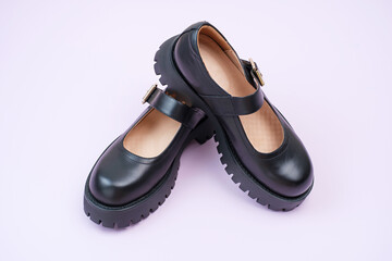 Pair of female black leather shoes on pink background close-up.