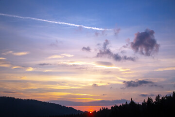 Colorful clouds in the sky at sunset against the backdrop of a mountainous forest area.