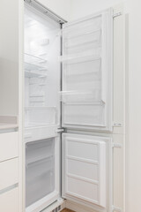 Photo of an open, empty and white refrigerator in a modern kitchen