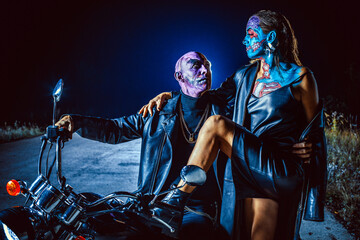 Photo of a demonic couple of zombie bikers on night road background. - obrazy, fototapety, plakaty