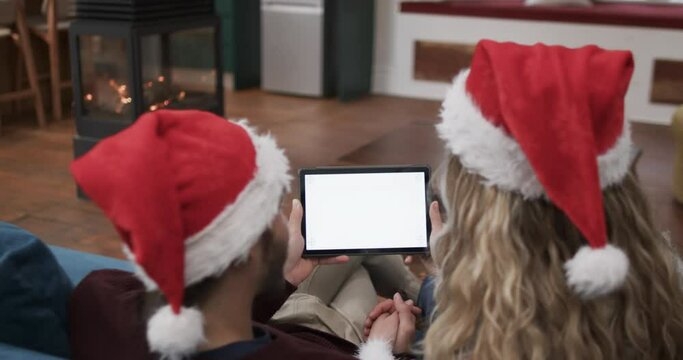 Diverse couple wearing santa hats using tablet with copy space on screen, in slow motion