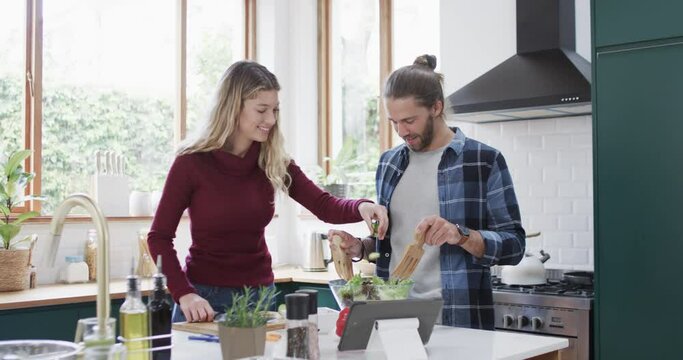 Happy diverse couple preparing dinner in kitchen using tablet at home, in slow motion