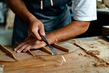 Close-up of guitar luthier using chisel to shave bracing of acoustic guitar.
