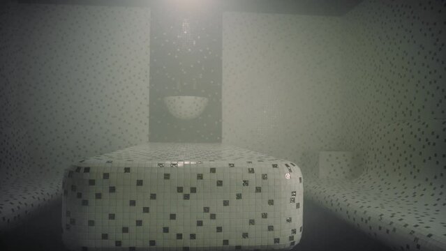 There is a dimly lit hammam with a modern tiled interior. The tiles are white and green, small in size. The Turkish sauna is empty, there is steam in the room.
