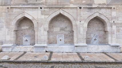 Fototapeta na wymiar External stone wall of 16th century historic Atik Valide Mosque with row of ablution fountains, located in Uskudar, Istanbul, Turkey, built by Nurbanu Sultan, the mother of Sultan Selim II