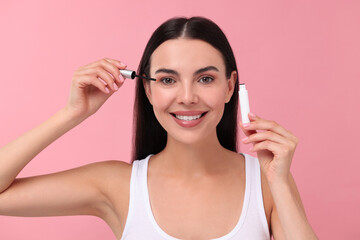 Fototapeta premium Beautiful woman applying serum onto her eyelashes on pink background. Cosmetic product