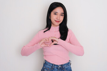 Asian young woman smiling and making heart shape symbol with hand on her chest