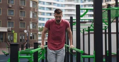 Athletic man doing dips at outdoor gym, low angle view. Camera moving backward and forward