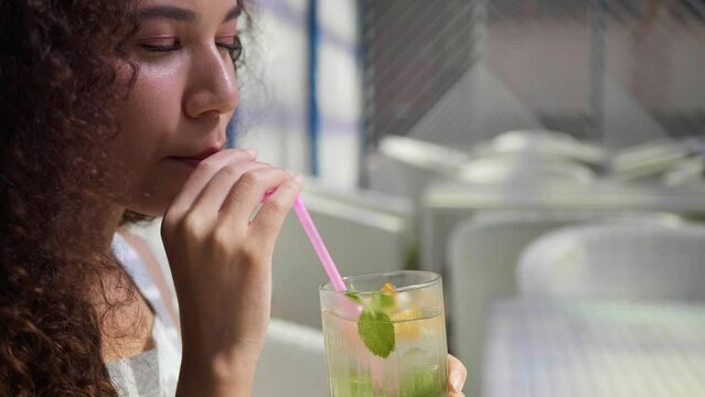 Beautiful young woman drinking refreshing lemonade at outdoor cafe, closeup. Slow motion effect