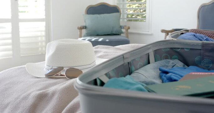 Close up of suitcase, hat and sunglasses on bed in bedroom, slow motion