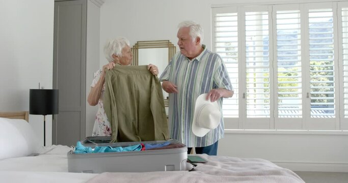 Senior caucasian couple packing suitcase in bedroom at home, slow motion