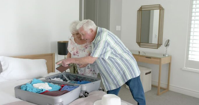 Senior caucasian couple packing suitcase in bedroom at home, slow motion