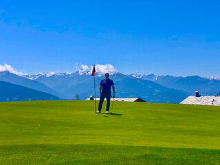 Fototapeta na wymiar Golfer Standing on Putting Green in Crans Sur Sierre Golf Course with Hole 7 and Mountain View in Crans Montana in Valais, Switzerland.