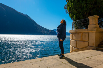 Woman Standing on a Terrace on the Waterfront with Mountain View over Lake Lugano in a Sunny Day in Lugano, Ticino, Switzerland.