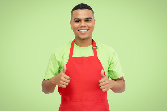 Latin american waiter with red apron on green background showing thumbs up