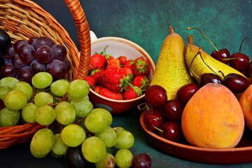 Harvest still life. Different sorts of bunches of grapes in basket, pears, peaches, handful of cherries in dish, strawberry in cup. Close up