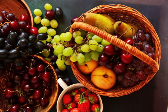 Harvest still life. Different sorts of bunches of grapes, pears, peaches in basket, handful of cherries in dish, strawberry in cup. Top view