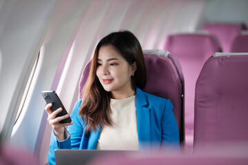 Young asian woman sitting on seat in airplane and talking by smartphone. Young woman traveller talking on cell phone