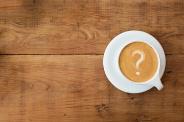 Top view of a cup of coffee with a question mark in the foam on a wooden table - obrazy, fototapety, plakaty