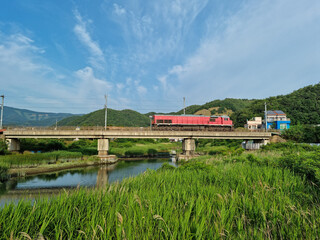 A rural scene with a red train crossing a bridge.