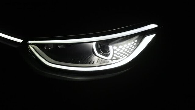 Headlight turning off switching of car LED headlights in night. New modern electric car headlamp. Close up of car front IQ Led Light with a Black Background