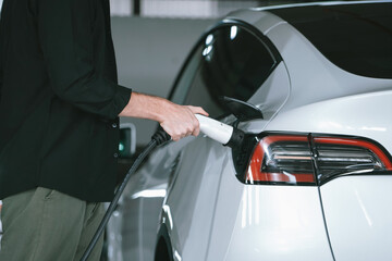 Young man travel with EV electric car to shopping center parking lot charging in downtown city...