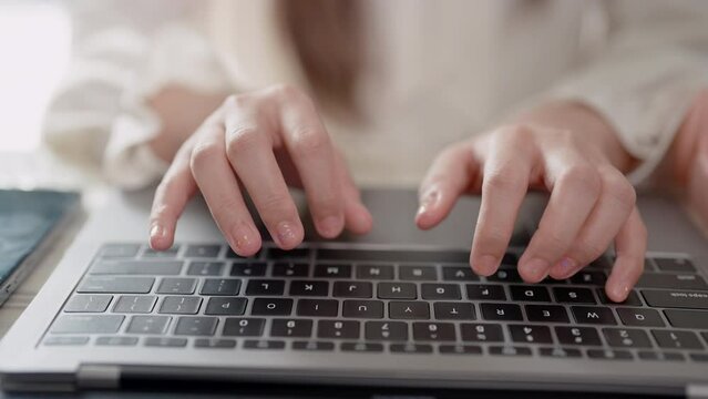Close-up of Asian woman's hand fingers pressing keyboard Sitting at home working on the bed. Typing with laptop keyboard, hands resting on computer, typing document with speed and accuracy.