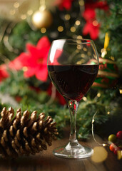 Glass of red wine on wooden table with Christmas decorations. Christmas tree and lights in the background.