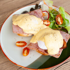 Eggs Benedict, breakfast and brunch, made from poached egg, English muffin,  ham, bacon, Hollandaise sauce and mixed salad 