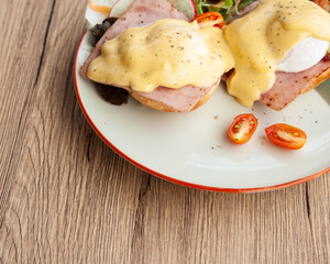 Eggs Benedict, breakfast and brunch, made from poached egg, English muffin,  ham, bacon, Hollandaise sauce and mixed salad 