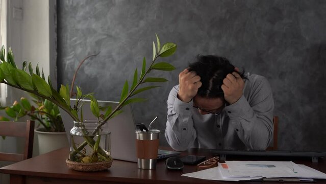 Frustrated businessman sitting on desk with hands on head in office. Tired and worried businessman in office workplace holding his head in hands after working late. Office interior.