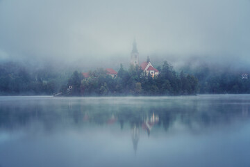 Famous alpine Bled lake (Blejsko jezero) in dense fog, amazing misty landscape, Slovenia. Scenic view of the lake, island with church and reflection in the water, outdoor travel background - obrazy, fototapety, plakaty
