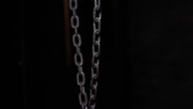 Close-up of hanging metal chains in a dark room, chains swinging from side to side. Quest room or horror room.