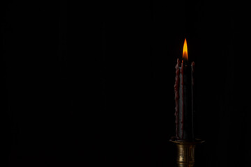Closeup of black candle burning in golden candlestick for Halloween, black background, horizontal, with copy space