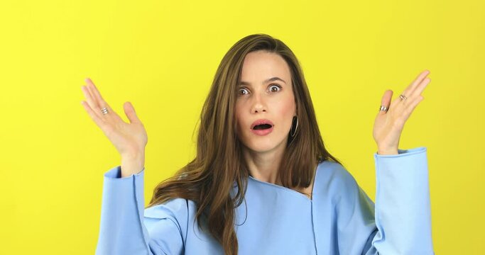 Close up of annoyed irritated young woman with an angry face looking furious, mad and feeling frustrated isolated on yellow background. Brunette girl expressions and emotions, wear blue sweater.