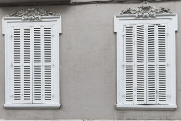 Fototapeta na wymiar Two wooden openwork windows with white shutters on the gray facade of the house. Ordinary life, home comfort, beautiful decoration of old houses.