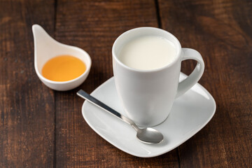 Milk in a porcelain cup and honey in a porcelain bowl on a wooden table