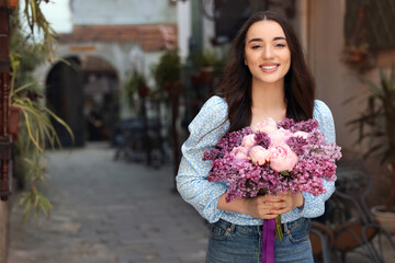 Fototapeta premium Beautiful woman with bouquet of spring flowers on city street, space for text
